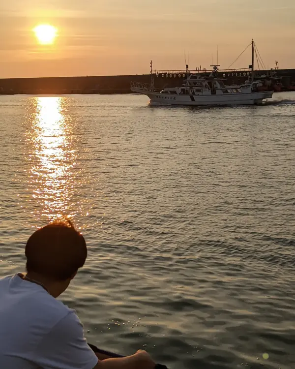 Sunset over a harbour, a boat heading out