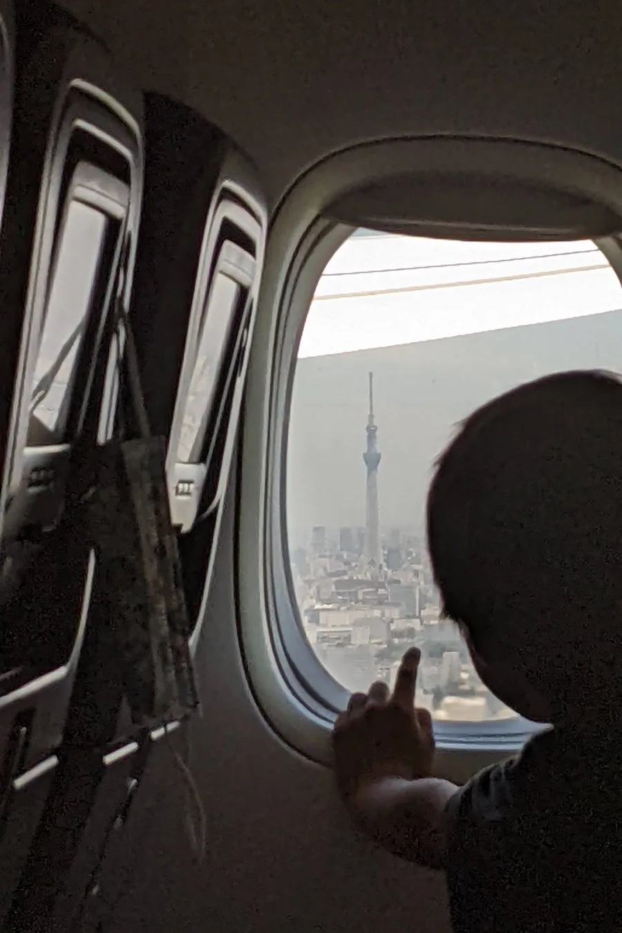 Tokyo from a plane window on the way out, the Skytree in the haze and a small hand pointing at it